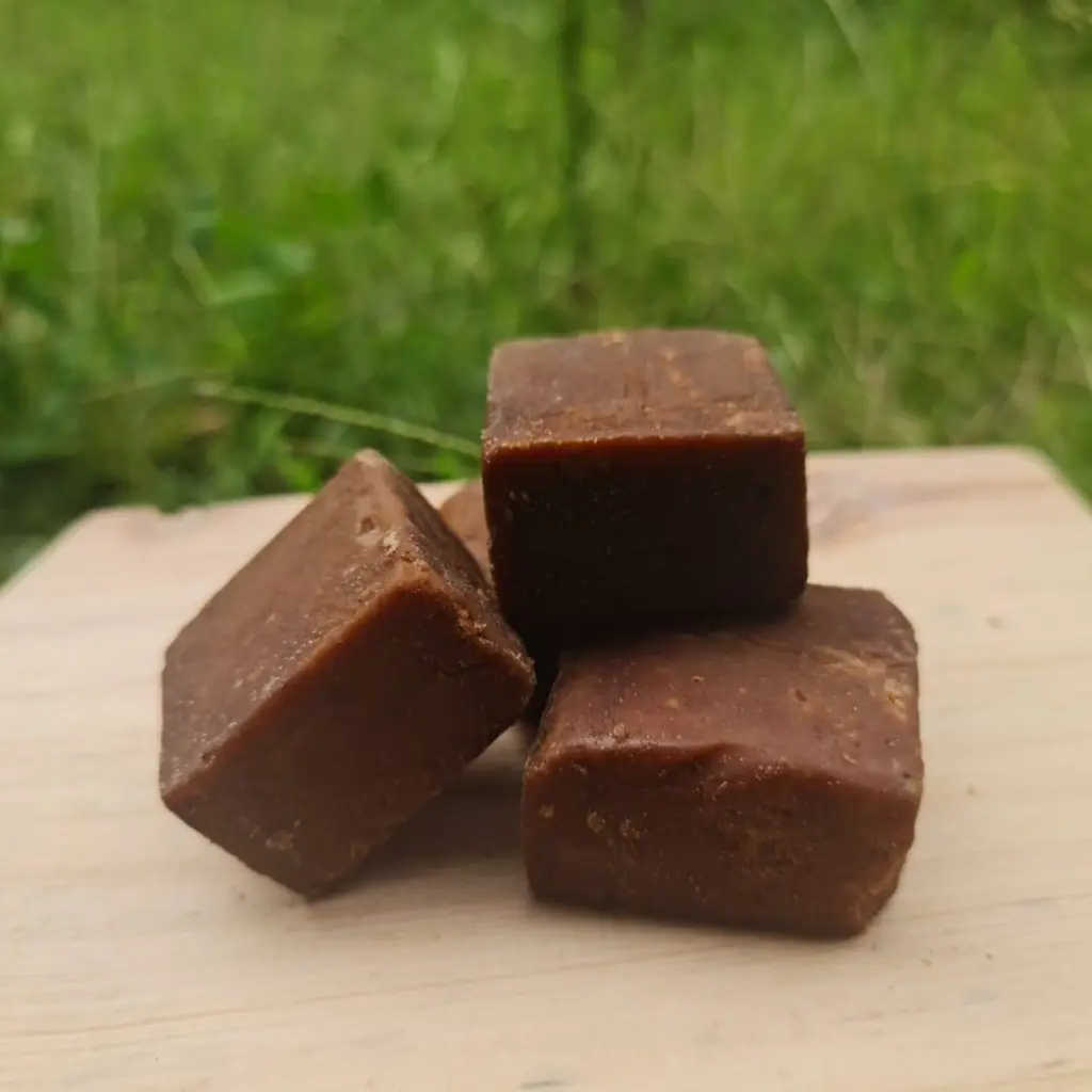 Cubes of brown organic coconut sugar stacked on a wooden board in a natural, green setting. Suitable for B2B wholesale and private label